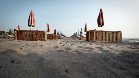 Empty beach in the seaside resort with folded sun loungers and umbrellas on a background of sunrise skyの写真素材