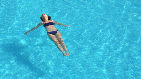 Young woman swimming in the crystal-clear pool laying on water surfaceの写真素材