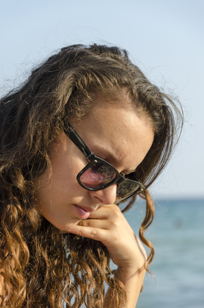 Woman with glasses thinking and looking down on a beach in summerの写真素材