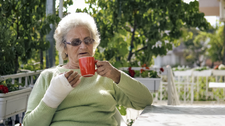 elderly old woman with injured hand drinking coffee outdoor sittingの写真素材