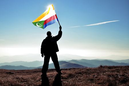 Successful silhouette man winner waving Comoros flag on top of the mountain peakの写真素材