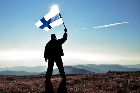 Successful silhouette man winner waving Finlandian flag on top of the mountain peakの写真素材