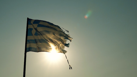Torn Greek flag waving backlit by summer beach sunrise sunの写真素材
