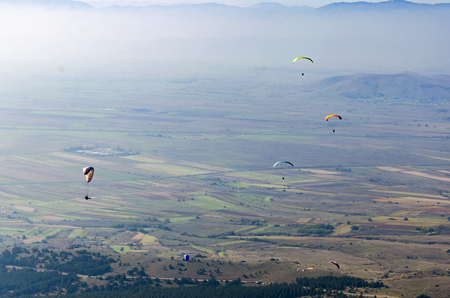 Paragliding in the mountains. Paragliders group fly over valley at sport competitionの写真素材