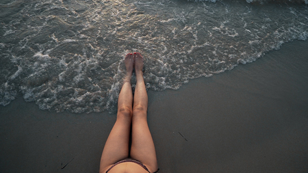 Top view of woman sexy legs on beach splashed by waves at sunsetの写真素材
