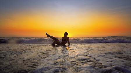 Sexy woman with perfect body sitting in ocean water at sunset on tropical beach. Cinematic steadicamの写真素材