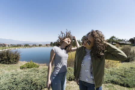 Two young friends having fun outdoors touching their curly hairの写真素材