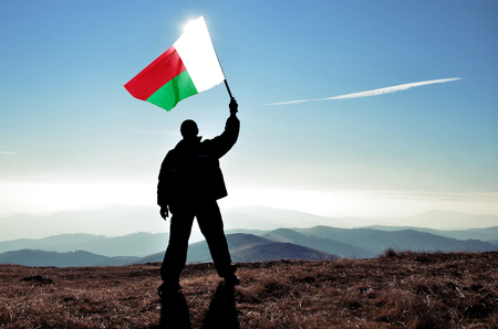 Successful silhouette man winner waving Madagascar flag on top of the mountain peakの写真素材