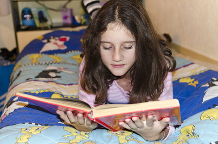 Little girl with reading book lying on bedの写真素材