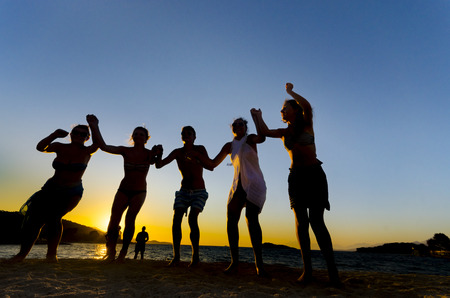 group of happy young people dancing at the beach on beautiful summer sunsetの写真素材