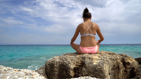 Woman doing yoga exercises on the beach with the sea in the background, crane shotの写真素材
