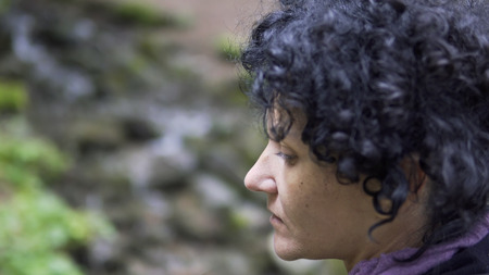 Close up portrait of hiker woman with curly hair looking up at forest observing a Route in natureの写真素材