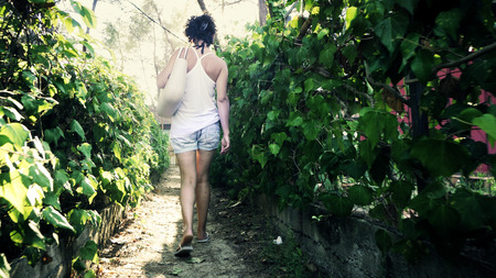 Fashion sexy female model in shirt and slippers walking to beach on narrow foliage passageの写真素材