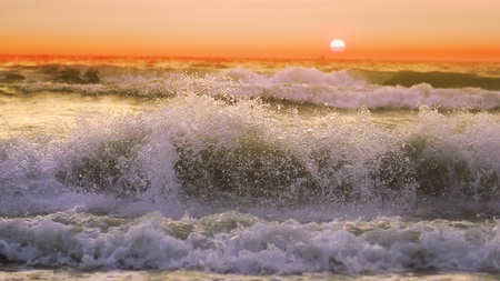 Sunset on the beach - Tranquil idyllic scene of a golden sunset over the sea, waves slowly splashing on the sandの写真素材