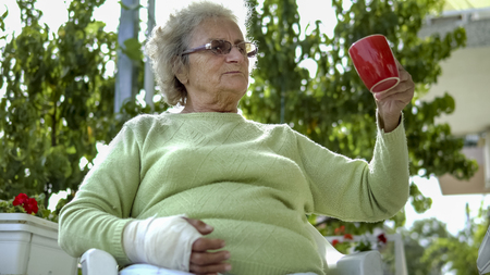 elderly old woman with injured hand drinking coffee outdoor sittingの写真素材