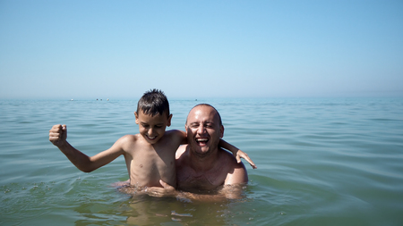 Father and son playing at beach together portrait fun happy lifestyle, boy embrace father and show victory successful gesturesの写真素材
