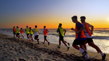 Football sport team is engaged in jogging training at sea at sunset. Thay make a run along the sea...