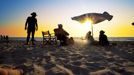 Elderly people silhouettes enjoy healthy vacation on beach with umbrella at sunset. Cinematic shotのeditorial素材