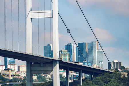 Detail of Bosphorus Bridge with background of Bosphorus strait and modern skyscraper buildings on a sunny dayの写真素材