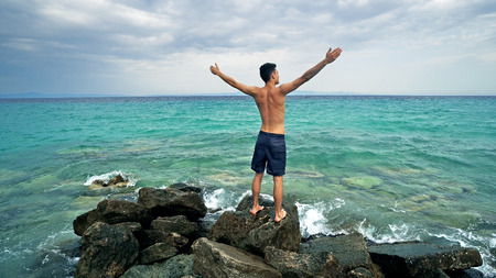 Teen Male makes a beach speech with hands open to sea, freedom conceptの写真素材