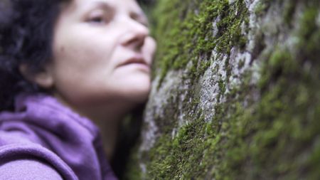 Emotional woman resting on the nature hand touching the stone moss in forest. Beautiful girl lying...