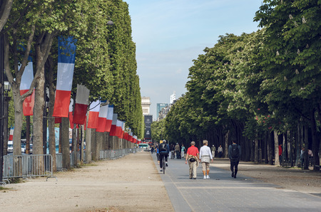 People walk down the Champs Elysees with French flags on trees waving celebrating national holliday in Paris, Franceのeditorial素材