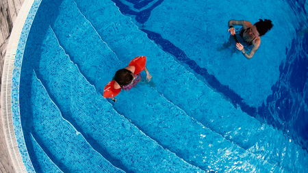 Top view of happy family, mother and daughter with arm bands smiling and splashing water to camera, slow motionの写真素材