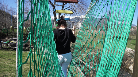 Teenage girl goes on hinged trail in extreme rope Park in summer forest. High-altitude climbing training of child on adventure trackの写真素材