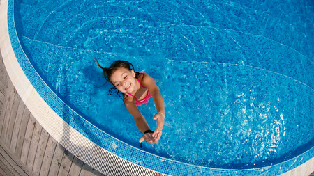 Little girl having fun standing in pool and splashing the camera, slow motion aerial viewの写真素材