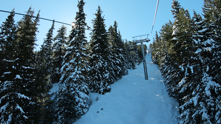 POV from ski lift with aerial view of skiers on slope and distant snow covered mountain peaksの写真素材