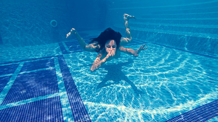 Attractive teen swimming underwater in luxury pool with closed nose by hand