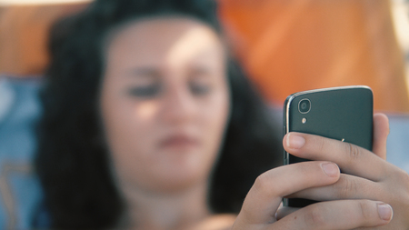 Female teen fingers type message on smartphone lying on beach sunbed