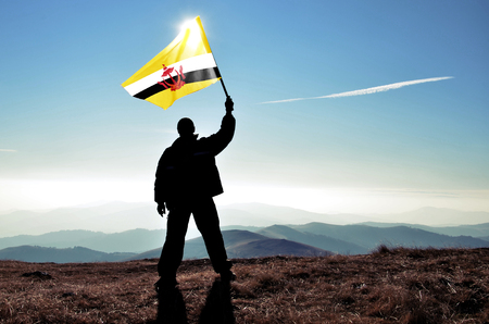 Successful silhouette man winner waving Brunei Darussalam flag on top of the mountain peakの写真素材