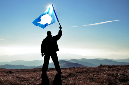 Successful silhouette man winner waving Antarctica flag on top of the mountain peakの写真素材
