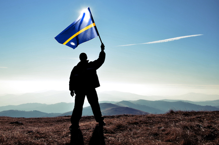 Successful silhouette man winner waving Nauru flag on top of the mountain peakの写真素材