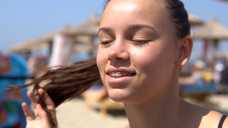 Beautiful happy teen girl with tooth braces smiling to camera sitting on beach during summer vacationの写真素材