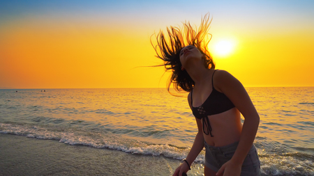 Beautiful model in swimsuit posing on the beach in sunset sunlight with long hair making formsの写真素材
