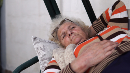 Elderly woman on porch swing bed lying and looking sad at distance