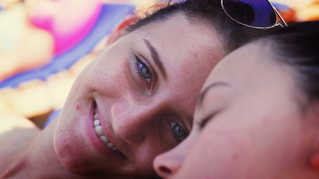 Closeup of two teen sleep on beach, open eyes and smile to camera