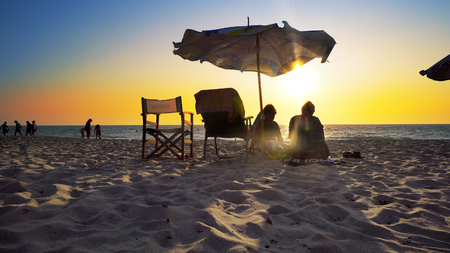 senior couple of old man and woman sitting on the beach watching sunsetの写真素材
