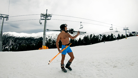 Naked nude male in shorts, helmet, goggles and boots standing on slope under ski liftの写真素材