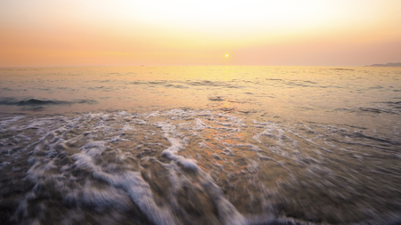 Sea waves crashing on beach at vibrant sunset at backgroundの写真素材