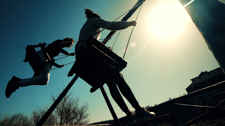 Two girls swinging on rope swing against sunrise sun. vintage cinematic lookの写真素材