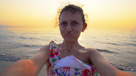 Selfie of young teen holding camera and turning on beach at sunsetの写真素材