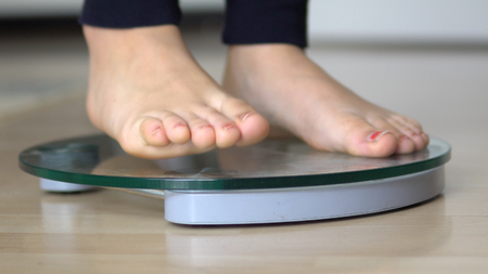 Girl feet on scales to measure the weight of the empty wooden floorの写真素材