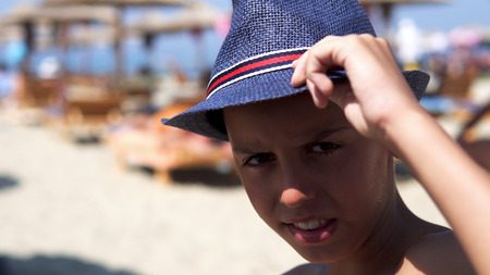 Handsome boy with hat look at camera and smile sitting on beach, cinematic dofの写真素材