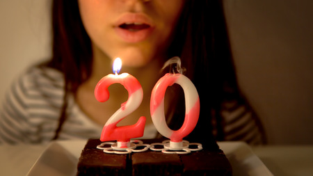 Girl blowing out a 20th birthday candle on a cupcakeの写真素材