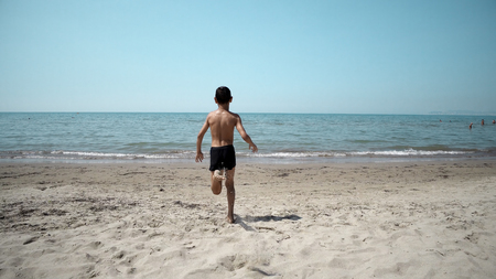 Happy boy getting int the sea water. Front cinematic steadicam viewの写真素材