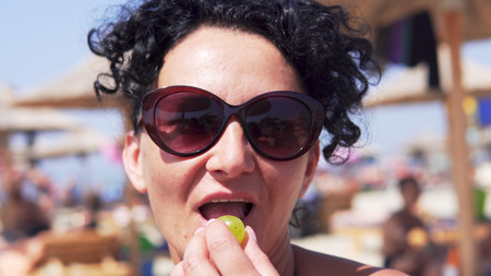 Close up portrait of a woman with glasses eating grape on beachの写真素材