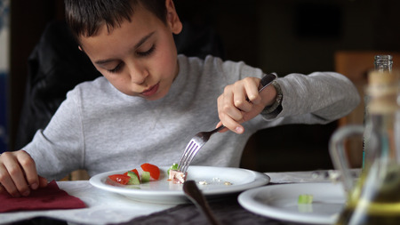 Handsome boy eats fresh vegetable salad with tomato, pepper, onionの写真素材